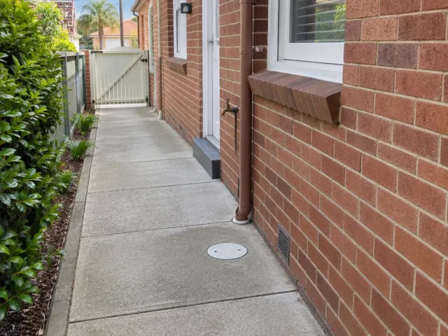 Brick side passage with a circular drain cover and dry concrete paving in Maroubra